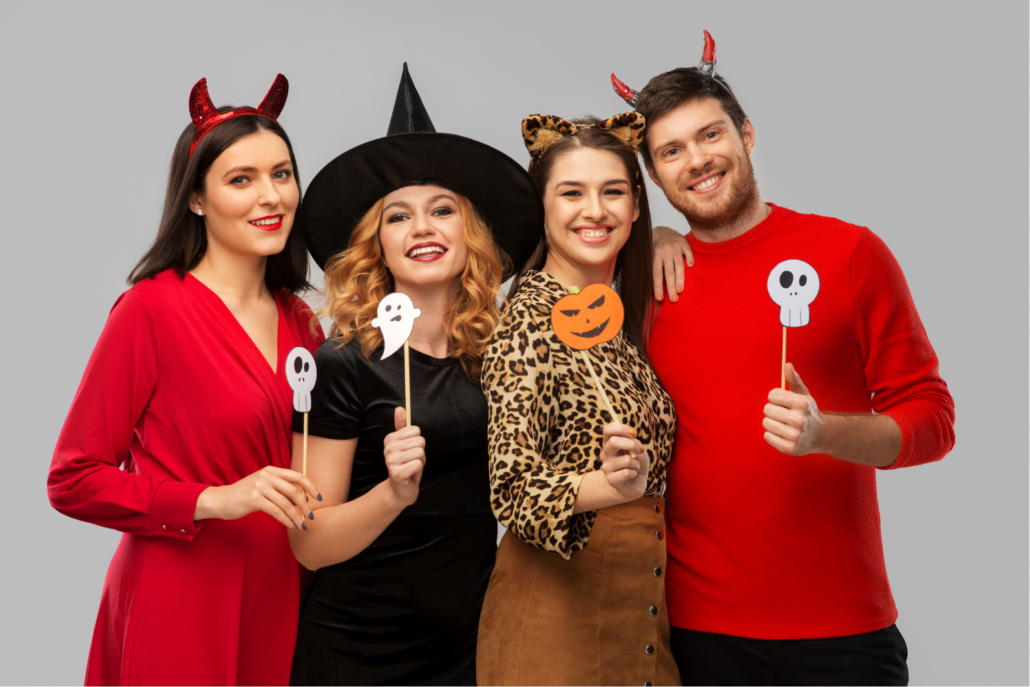 A group of four adults wearing costumes adapted from regular clothes pose for a picture holding Halloween accessories.