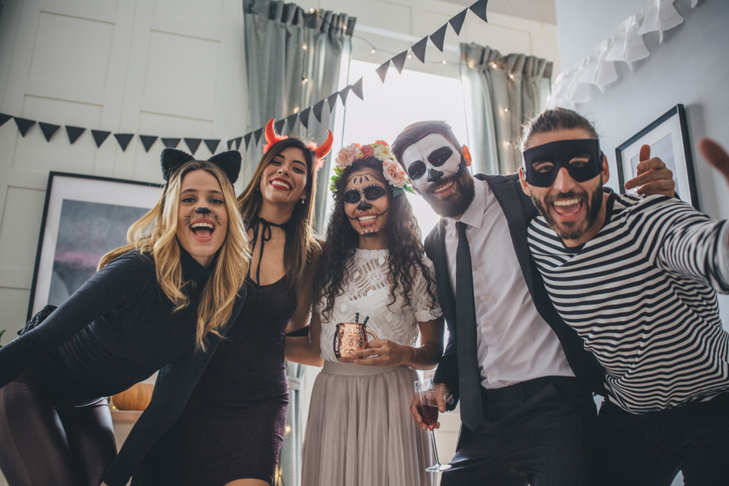 A group of five adults in Halloween costumes pose for a picture at a party.