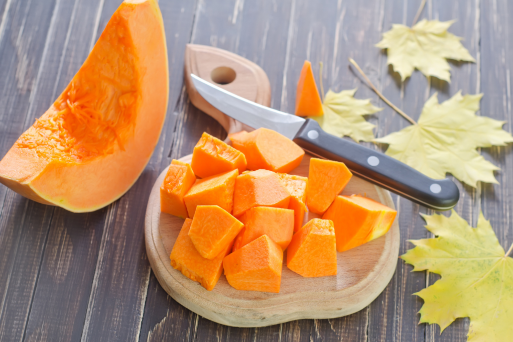 Chunks of cut up Pumpkin on a chopping board with a knife laying next to them.